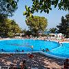 Piscina esterna con molti bagnanti e alberi intorno.