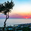 Tramonto sul mare con un albero in primo piano e un villaggio costiero.