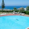 Piscina tonda con vista sul mare e sedie a sdraio bianche, pochi alberi e cielo sereno.
