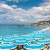 Spiaggia affollata con ombrelloni blu e bianchi, mare azzurro.