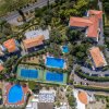 Complesso con piscine, campi da tennis e edifici con tetti rossi immerso nel verde.