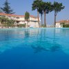 Piscina con edifici bianchi e tetti rossi sullo sfondo, circondata da alberi.