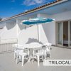 Terrazza con tavolo, sedie bianche e ombrellone blu. Sfondo di pareti bianche e porta a vetri.