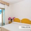 Camera con letto matrimoniale, testiera gialla, fiori rosa su comodino, vista su balcone e mare.