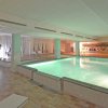 Piscina interna illuminata con lettini intorno e un grande murale sullo sfondo.