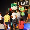 Bambini circondano una mascotte verde su un palco con la scritta 