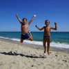 Due bambini felici saltano sulla spiaggia davanti al mare.