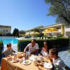 Famiglia fa colazione all'aperto vicino a una piscina con ombrelloni gialli.
