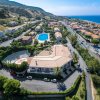 Vista aerea di un complesso con piscina, edifici e strada costiera vicino al mare.