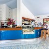 Un bar moderno con bancone blu, pavimenti decorati, un cameriere e due clienti seduti su sgabelli.