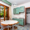 Cucina con mobili verde acqua, tavolo rotondo bianco, sedie legno, finestra grande con tende beige.