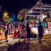 Bambini e adulti seduti e in piedi davanti a un palco all'aperto, osservano uno spettacolo serale.