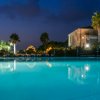 Piscina blu di sera con palme e un edificio in pietra sullo sfondo.