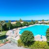Una grande piscina circondata da lettini e ombrelloni, con vista sul mare tra le palme.