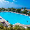 Piscina affollata con bagnanti, lettini e ombrelloni, e vista sul mare.