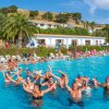 Gruppo di persone che ballano in una piscina circondata da sdraio e ombrelloni.