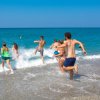 Un gruppo di persone corre verso le onde del mare limpido su una spiaggia sabbiosa.