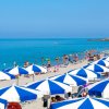 Vista di una spiaggia con ombrelloni blu e bianchi e molte persone in acqua.
