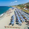 Spiaggia con ombrelloni blu e bianchi, persone in relax e mare azzurro.