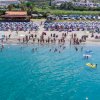 Spiaggia affollata con persone in acqua, ombrelloni in fila e chiosco.