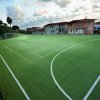Campo sportivo all'aperto circondato da reti, con case sullo sfondo e cielo nuvoloso.