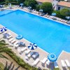 Piscina azzurra con ombrelloni blu e bianchi, circondata da lettini e vegetazione.