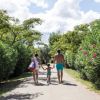 Famiglia cammina su un sentiero tra alberi e fiori.