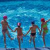 Quattro bambini si tuffano in una piscina tenendosi per mano.