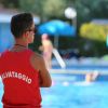 Bagnino di spalle in maglia rossa osserva la piscina.