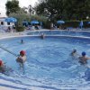 Persone nuotano in piscina circondata da ombrelloni blu.