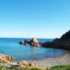 Spiaggia di ciottoli con mare calmo e scogliera.