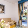 Salotto con divano beige, tende blu e gialle. Finestra aperta su balcone con vista piscina.