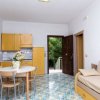 Cucina-soggiorno con mobili gialli, tavolo rotondo, divano beige. Porta aperta su area verde.