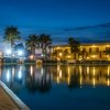 Piscina notturna con palme e luci, edificio illuminato sullo sfondo.
