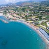 Vista aerea di una spiaggia con mare azzurro, stabilimenti balneari e colline sullo sfondo.