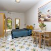 Camera con pareti bianche, letto, tavolo e sedie, pavimento decorato e grande quadro.