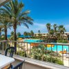 Vista dalla terrazza di una piscina con palme e ombrelloni arancioni.