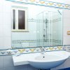 Un bagno con lavandino, specchio grande, decorazioni floreali azzurre e gialle sulle piastrelle.