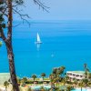 Vista su un mare blu con una vela bianca, vicino a un resort con piscina e palme.