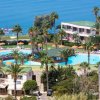 Panoramica di un resort con piscina circondata da palme vicino al mare.
