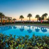 Piscina illuminata al tramonto con sedie a sdraio e palme sullo sfondo.