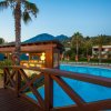 Piscina con ponte in legno, palme e vista su montagne al tramonto.