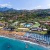 Spiaggia affollata con ombrelloni colorati, mare turchese e montagne sullo sfondo.