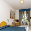 Stanza d'albergo con letto matrimoniale, mobili gialli, e tende a righe blu e gialle.