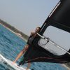 Dettaglio di persona in windsurf vicino alla riva con mare blu e spiaggia sullo sfondo.