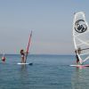 Tre persone praticano windsurf su un mare calmo con vele colorate.