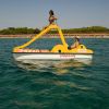 Due persone su un pedalò giallo in mare con costa verde sullo sfondo.