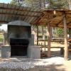 Barbecue in muratura accanto a tavoli da picnic coperti in un'area verde.