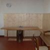 Un tavolo di legno con sedie in una stanza semplice, pareti bianche e una mensola di legno chiaro.