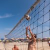 Partita di beach volley con giocatori, rete e cielo limpido.